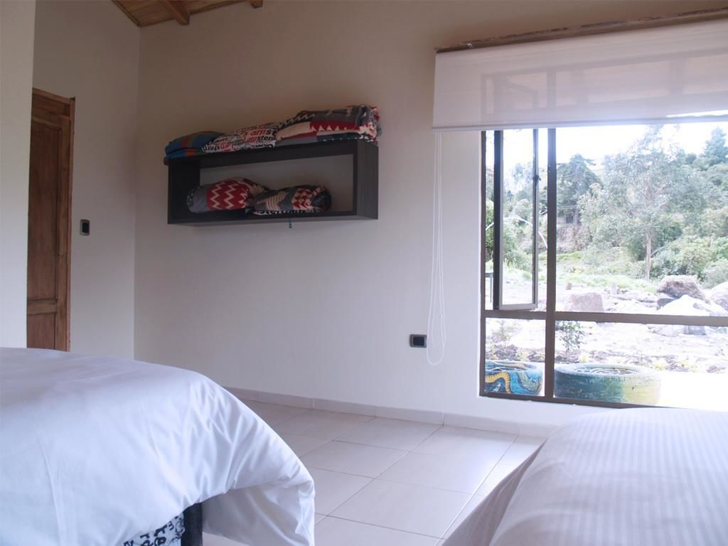 A room with two beds, a window with a view of greenery, and a shelf with folded blankets.