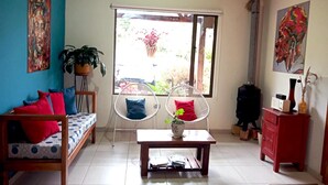 A cozy living room with a sofa, two white chairs, a small table, and a window with a view of greenery. - Villa Cucha (Monguí)