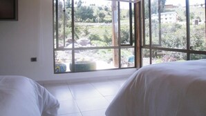 A bedroom with two beds, a large window with a view of a garden and buildings. - Villa Cucha (Monguí)