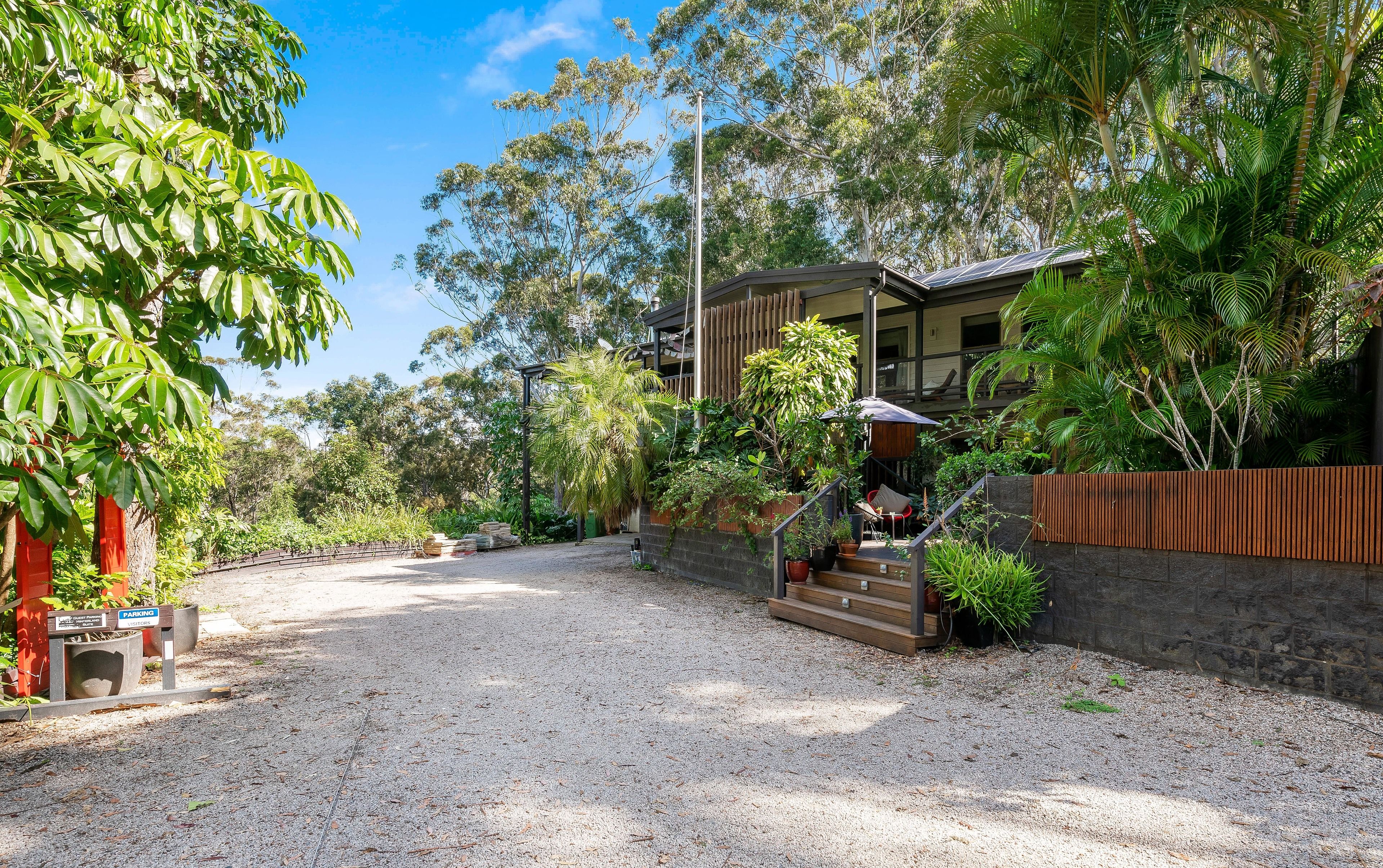 A residential area with a gravel driveway, a wooden fence, and a house with a balcony.