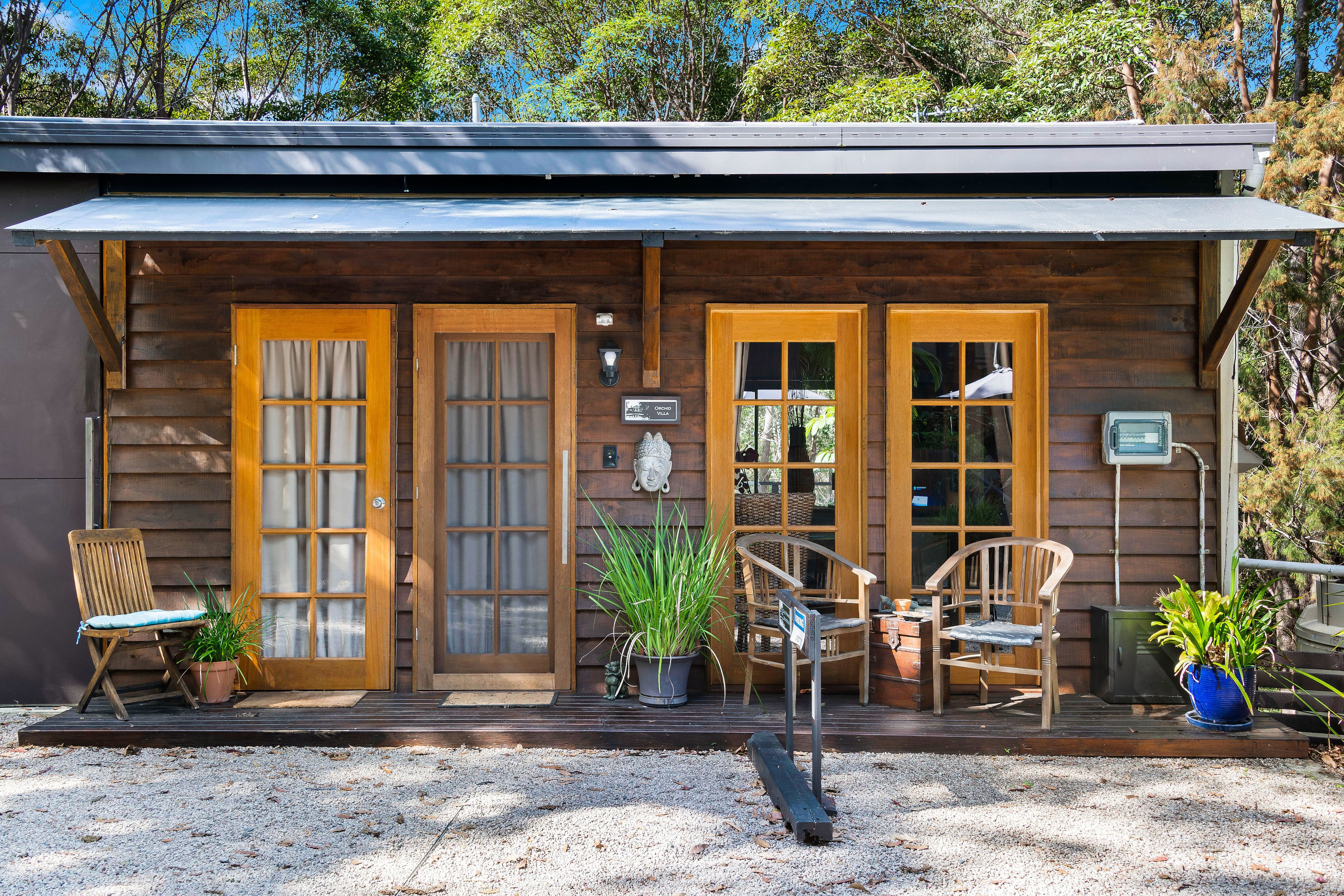Une cabane en bois avec deux portes d’entrée, une véranda avec des chaises et des plantes en pot.