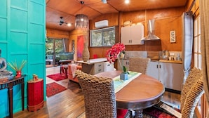 A modern kitchen with wooden cabinets, a dining area with woven chairs, and a ceiling fan.