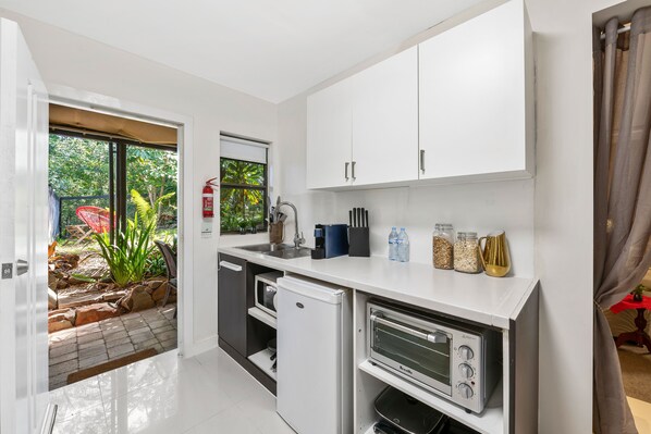 A compact kitchen with white cabinets, a built-in oven, and a small refrigerator. - Noosa Hinterland Retreat (Tinbeerwah)
