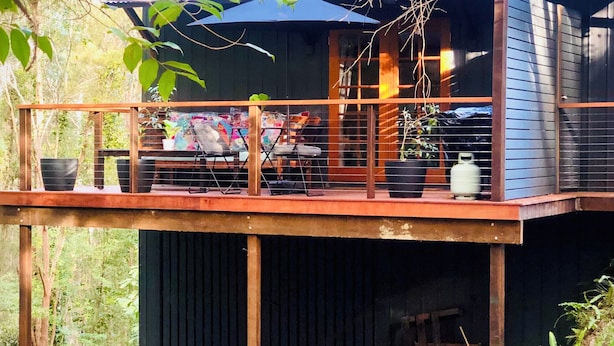 A wooden deck with a table and chairs, surrounded by greenery.