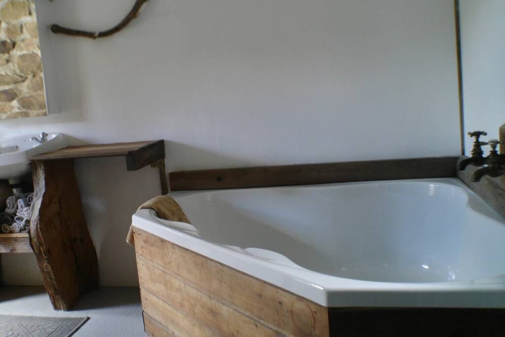 A wooden bathtub with a white interior, a stone wall, and a wooden shelf with items.