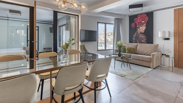 Una sala de estar moderna con una mesa de comedor de vidrio, asientos cómodos, un amplio ventanal con vista a la ciudad y una lámpara de araña contemporánea.