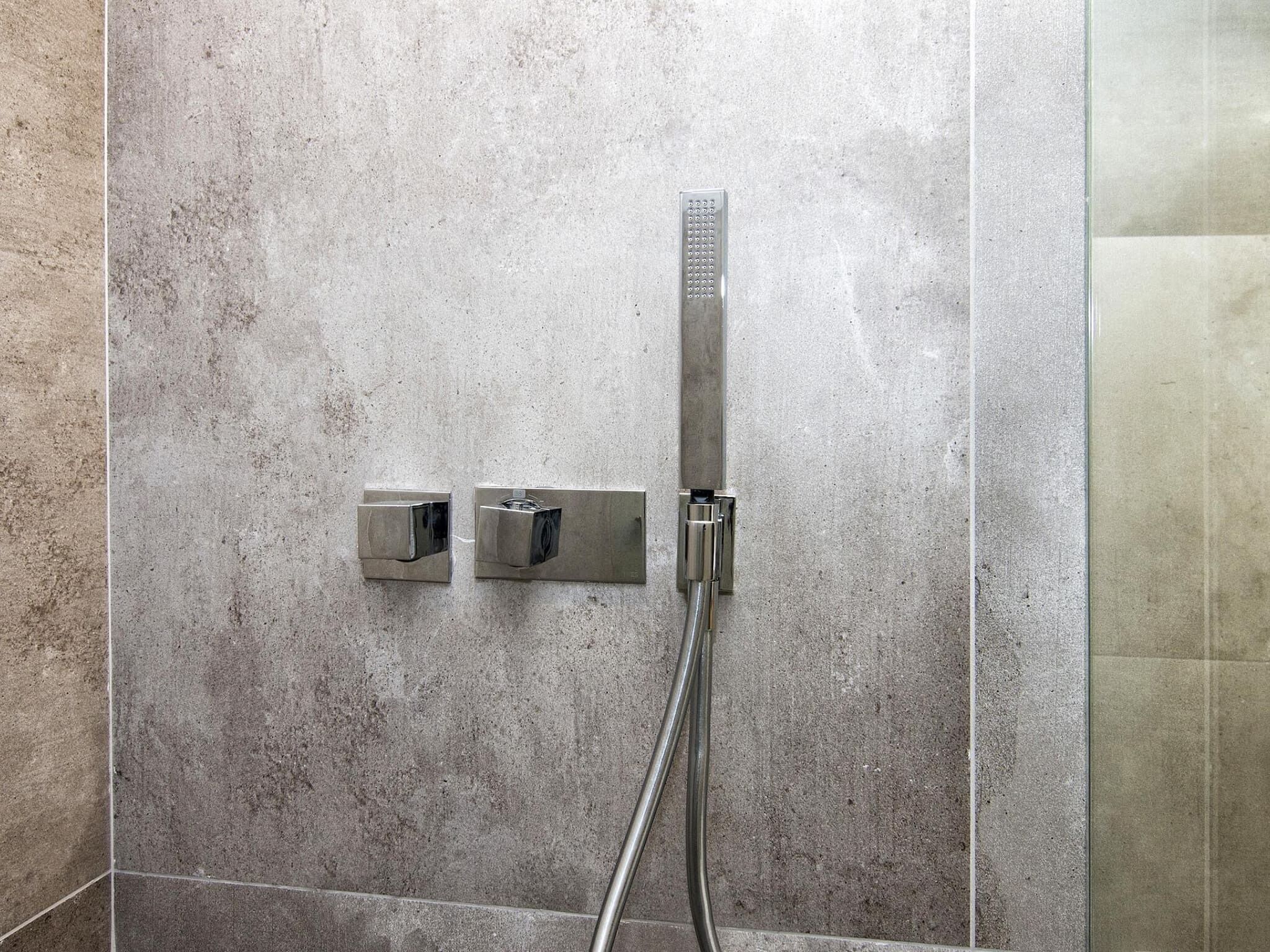 A shower with a handheld showerhead and two wall-mounted controls.