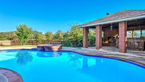 A backyard with a swimming pool, a hot tub, and a covered patio area.