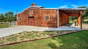 A rustic barn-style building with a covered porch, a large wooden door, and a small wheel.