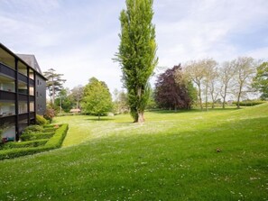 Un bâtiment moderne doté d’un balcon, entouré d’une pelouse bien entretenue et d’arbres.