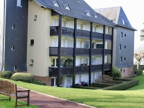 A multi-story residential building with balconies, a paved pathway, and a bench. - Le Parc de la Chaumière by Interhome (Deauville-Trouville)