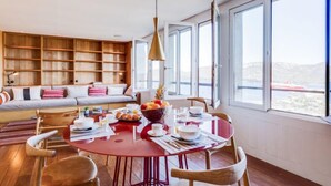 Un espace repas moderne avec une table rouge, des chaises en bois et une bibliothèque en arrière-plan.