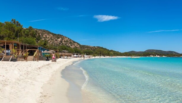 Une plage avec une eau turquoise et limpide, du sable blanc et une structure en bois avec des marches descendant vers la plage.