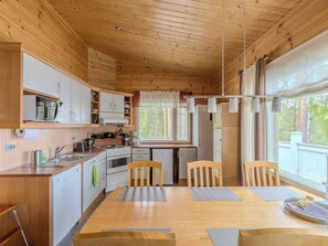 A wooden cabin interior with a kitchen, dining area, and a window overlooking a forest.
