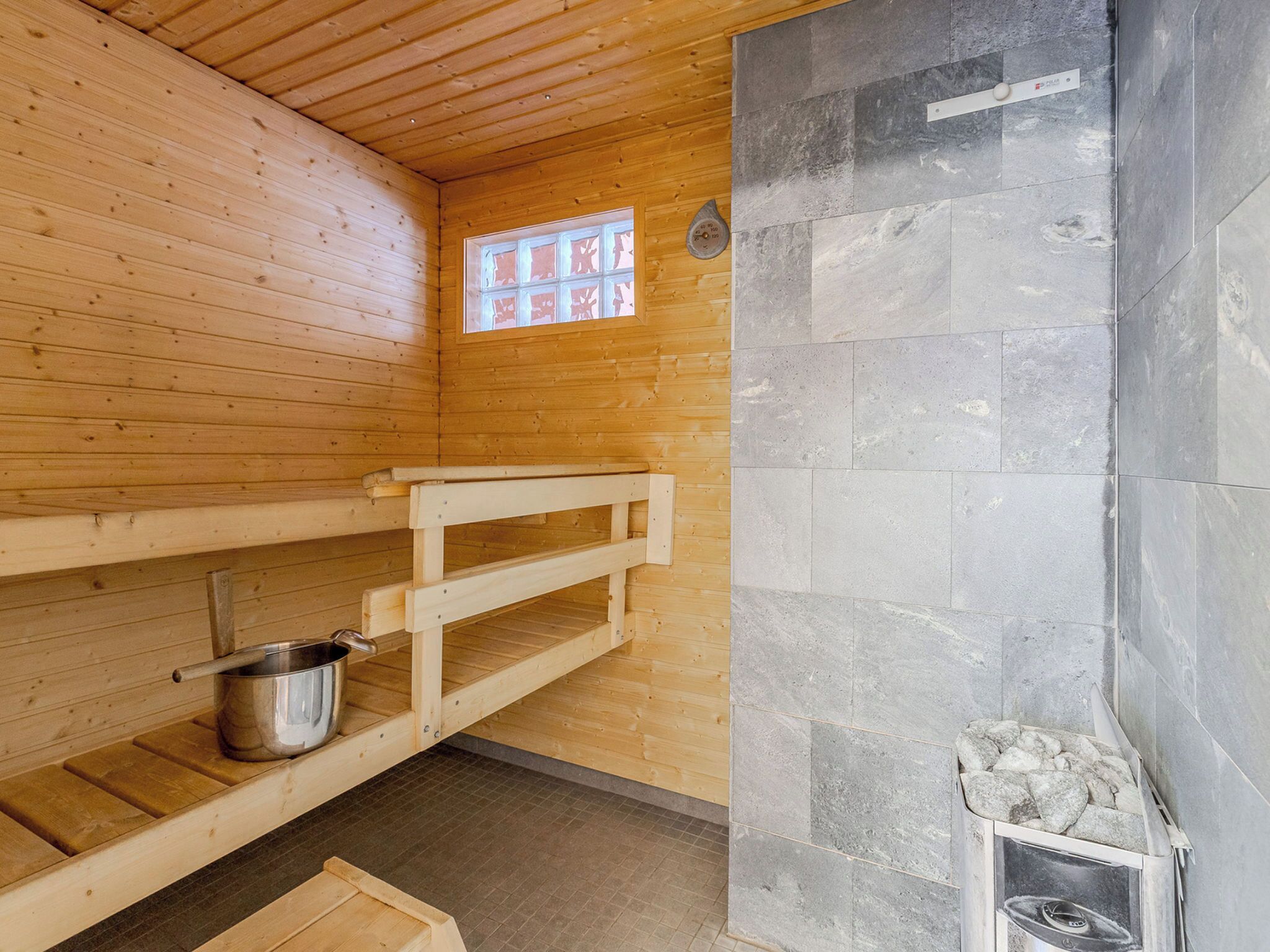 A sauna room with wooden benches, a stone wall, and a window.