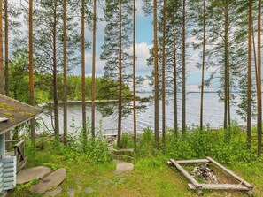 A cabin with a stone staircase leading to a dock, surrounded by tall pine trees and a lake.