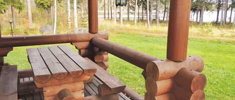 Un tavolo da picnic in legno con panche e un parapetto, su un patio con vista su una foresta e un lago.