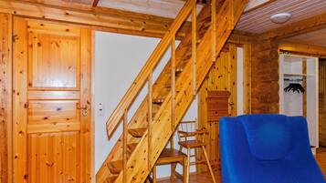 A wooden staircase leading to an upper level, a wooden door, a chair, and a blue sofa in a room with wooden walls and tiled flooring.