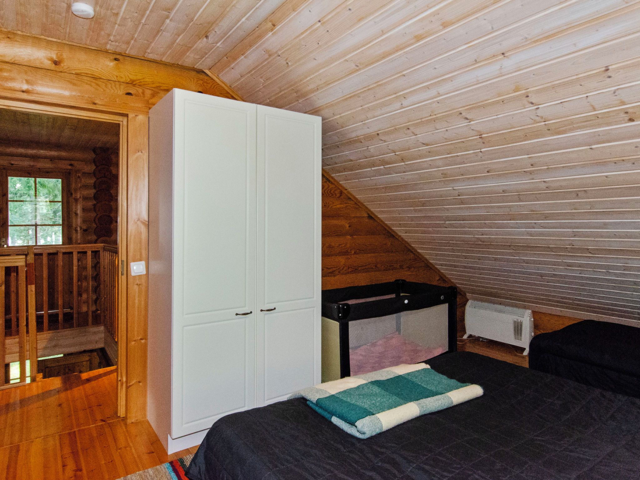 Una camera da letto con soffitto spiovente, un armadio bianco, un letto con copriletto e una finestra vista verde.
