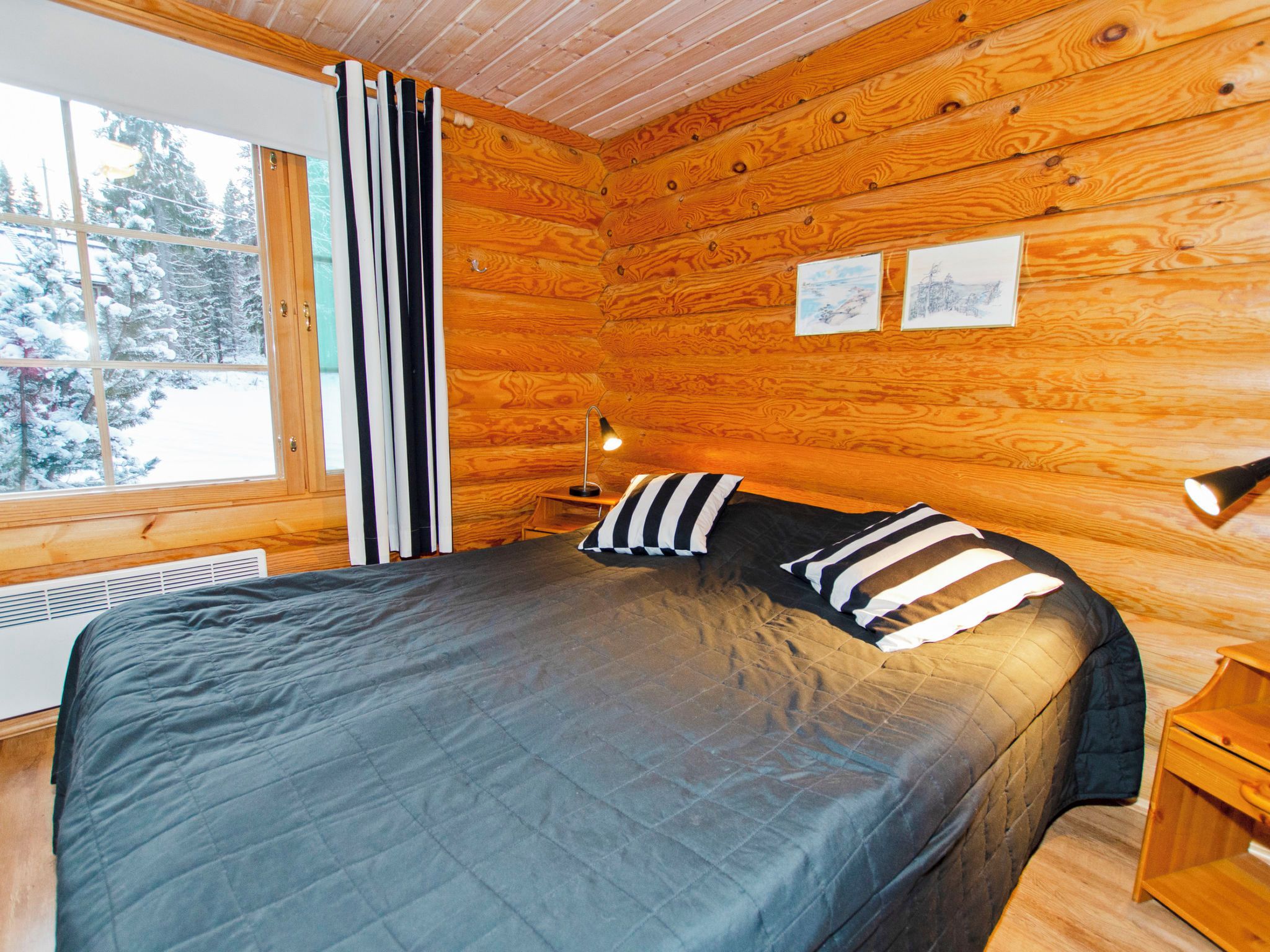 A wooden cabin bedroom with a bed, a nightstand, a lamp, and a window with curtains.