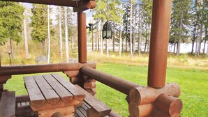 A wooden picnic table with benches, surrounded by a wooden deck and a forested area in the background.