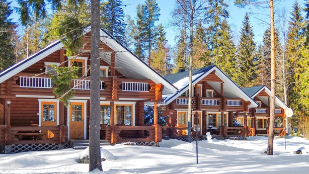 A log cabin resort with multiple buildings, wooden balconies, and a snowy landscape.