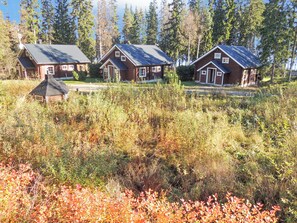 A row of three wooden cabins with sloped roofs, surrounded by dense forest and autumn foliage.