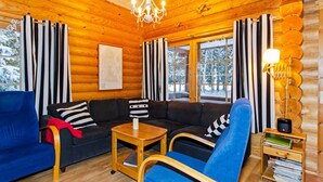 A cozy log cabin interior with a sofa, blue armchair, wooden coffee table, and a lamp.