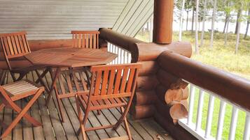 A wooden deck with a table and chairs, surrounded by a railing and a view of trees.