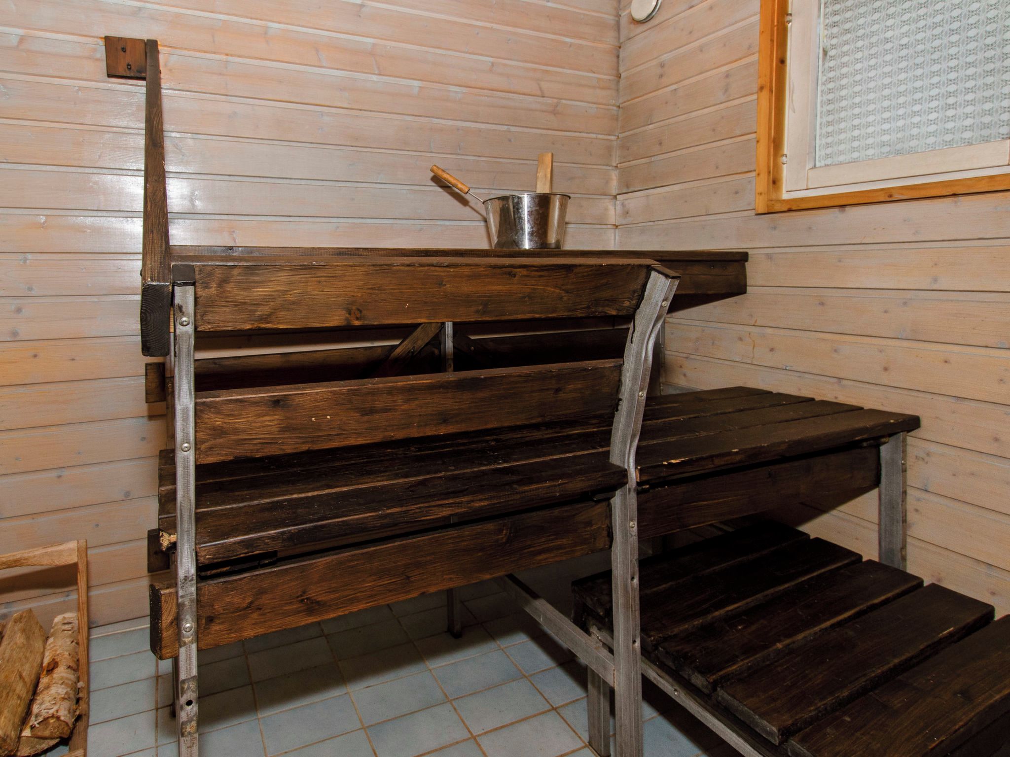Una banca de fusta amb suports metàl·lics en una habitació de parets de fusta i terra emblenquinada.