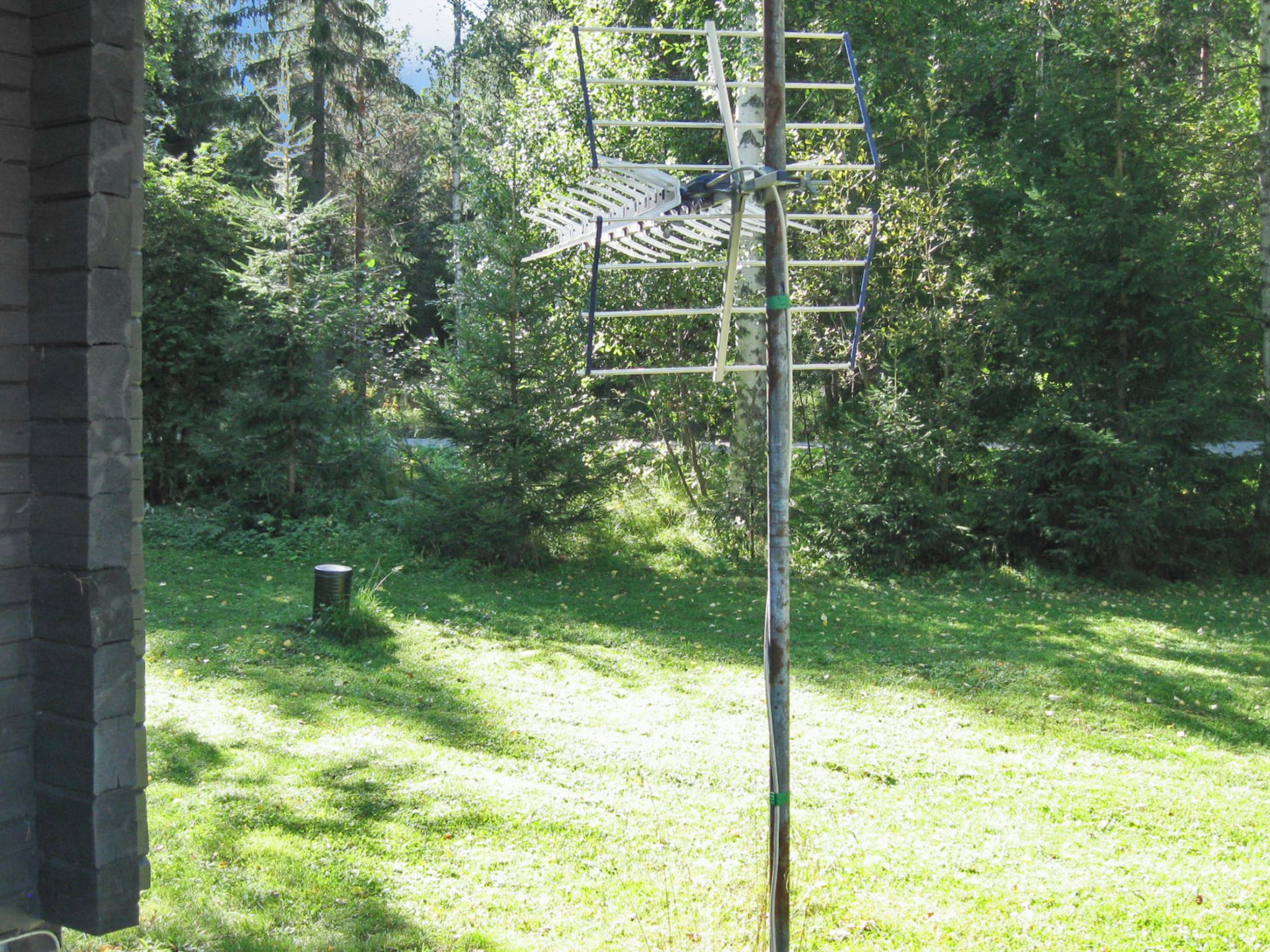 A metal antenna structure in a grassy area with trees in the background.
