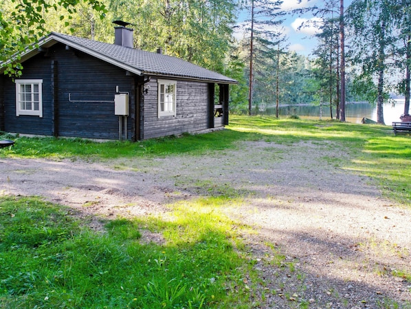 A rustic cabin with a porch, surrounded by a grassy area and trees.