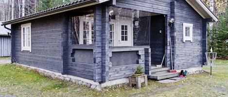 Een houten hut met een veranda, schoorsteen en een kleine tuin.