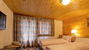 Une pièce avec un plafond et des murs en bois, deux lits avec du linge de lit blanc, un bureau avec une chaise et une lampe sur une table de chevet.