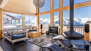 A modern interior with a sofa, a lounge chair, a TV, and a fireplace, with a mountain view through large windows. - Woovim 8 by Interhome (Nendaz)