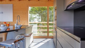 A modern kitchen with wooden beams, a large window, and a view of greenery. - Woovim 8 by Interhome (Nendaz)