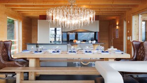 A wooden interior with a dining table set for six, a chandelier, and a kitchen in the background. - Woovim 8 by Interhome (Nendaz)