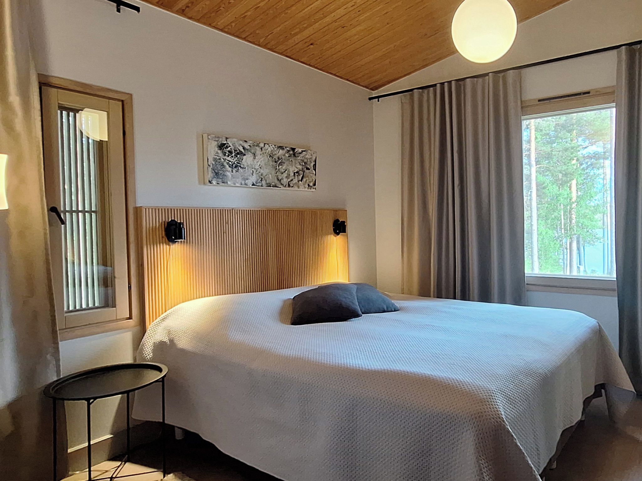 Ein Schlafzimmer mit einem Bett, einem Nachttisch, einem Fenster mit Vorhängen und einer Deckenleuchte.