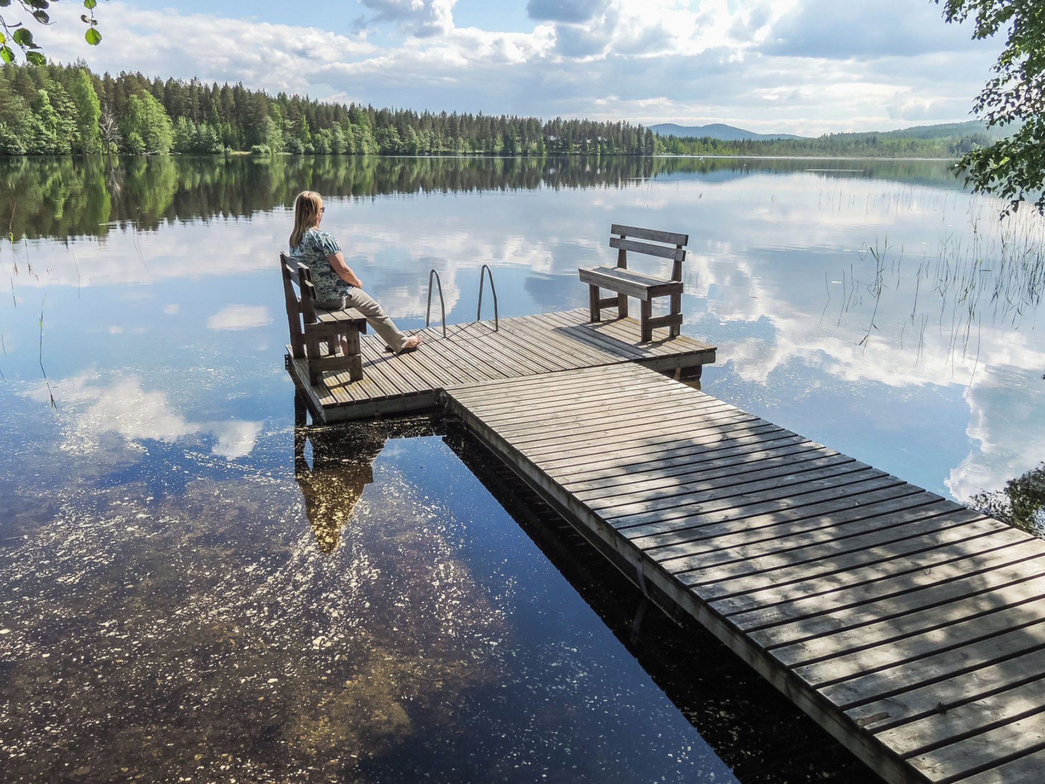 A wooden dock extending into calm water with a person sitting on a bench.