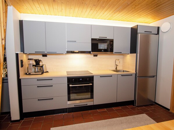 A modern kitchen with grey cabinets, a built-in oven, a microwave, and a stainless steel refrigerator.
