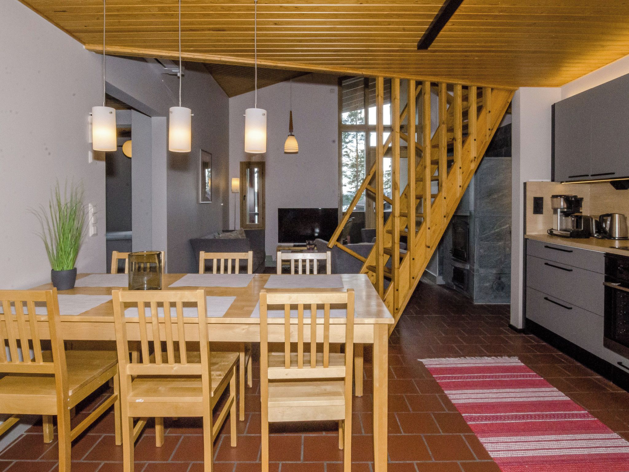 Una cocina moderna con armarios de madera, un comedor con mesa y sillas de madera, y una escalera con barandilla de madera.