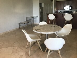 Een moderne keuken met witte kasten, een roestvrijstalen koelkast en een inbouwoven. Er staat een rond marmeren tafel met vier witte stoelen.