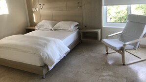 A modern bedroom with a bed, bedside tables, a chair, and a window.