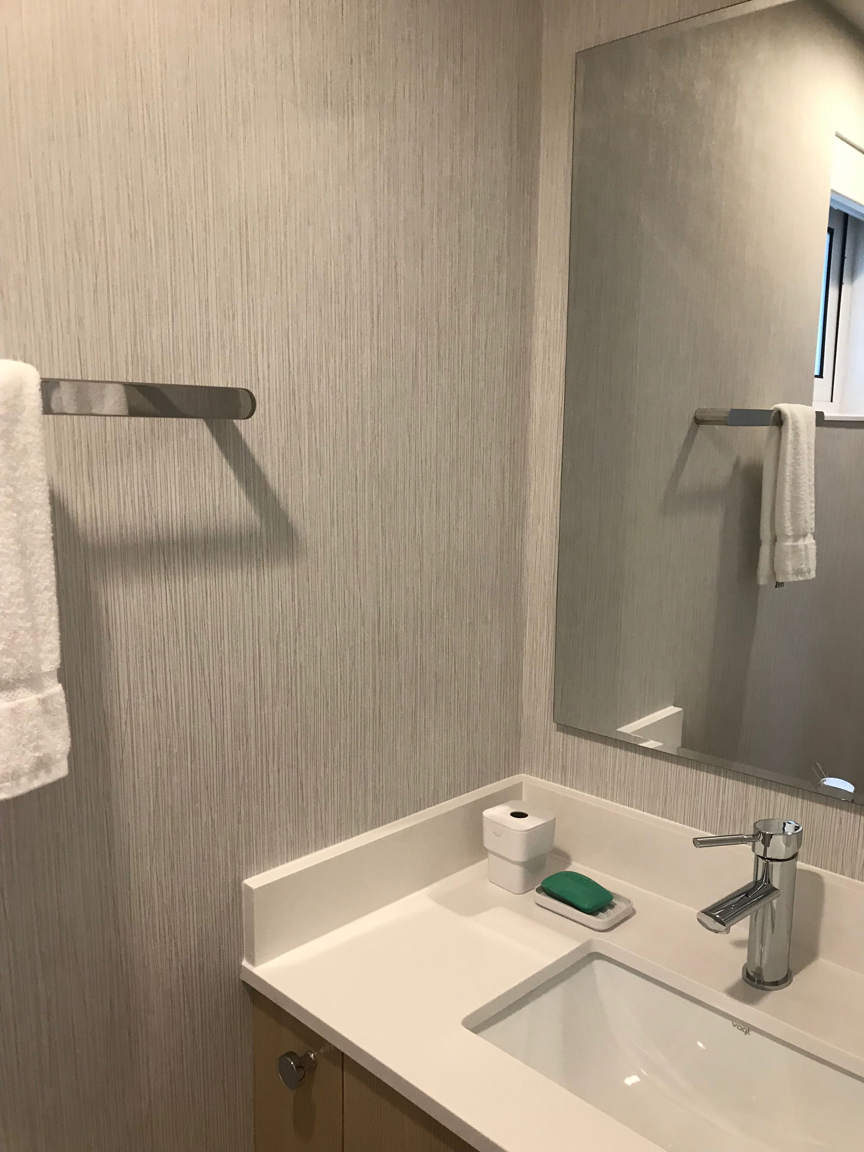 A bathroom with a white sink, a mirror, a towel rack, and a toilet paper dispenser.
