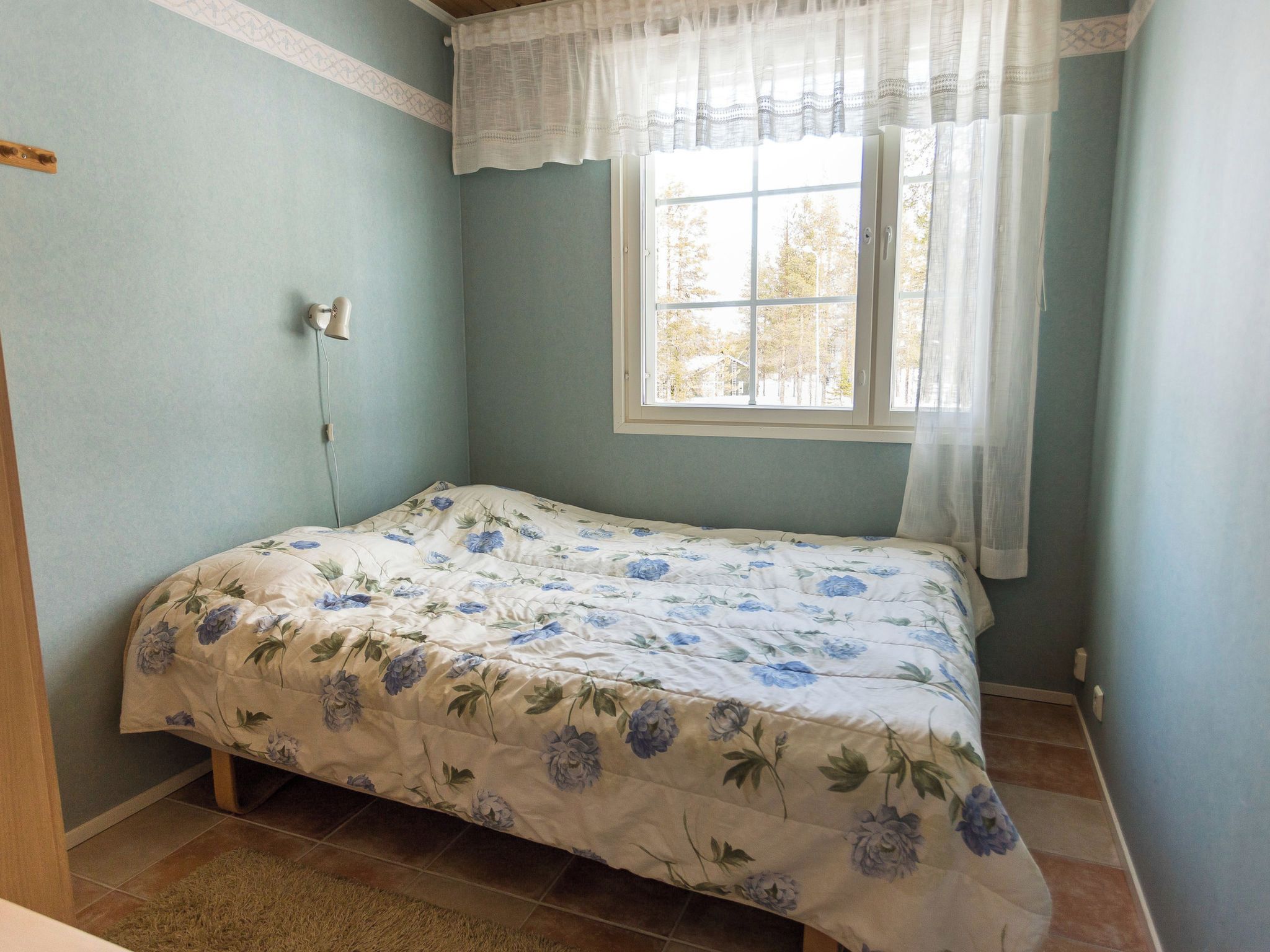 Une chambre à coucher avec un lit, une fenêtre avec des rideaux et une lampe fixée au mur.
