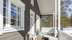 A covered porch with a white railing, a wooden bench, and a white plastic chair.
