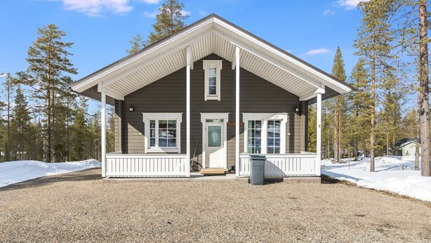 A two-story lodge with a porch, surrounded by a forest and snow.