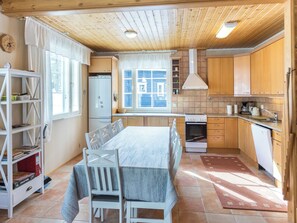 A kitchen with wooden cabinets, a dining table with chairs, a refrigerator, an oven, and a window with curtains.