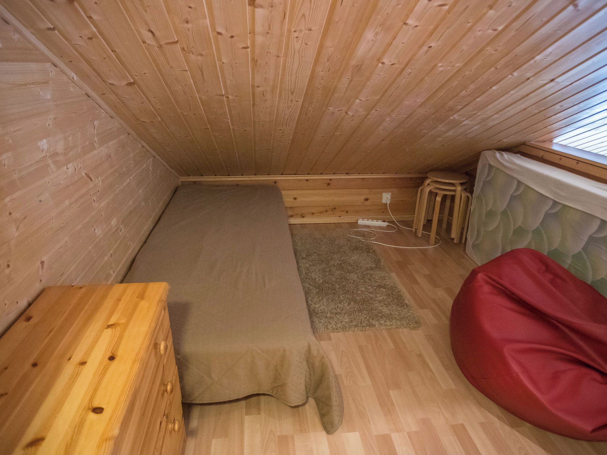 Una habitación pequeña y acogedora con una cama litera de madera, una mesa de madera individual, un sillón de peluche rojo y una ventana con persianas.