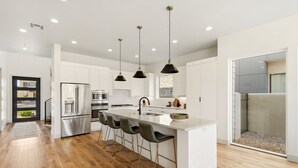 A modern kitchen with a central island, bar stools, stainless steel appliances, pendant lighting, and a view through a glass door. - Golf Course Views, Private Pool, Hot Tub, Fire Pit (Washington)